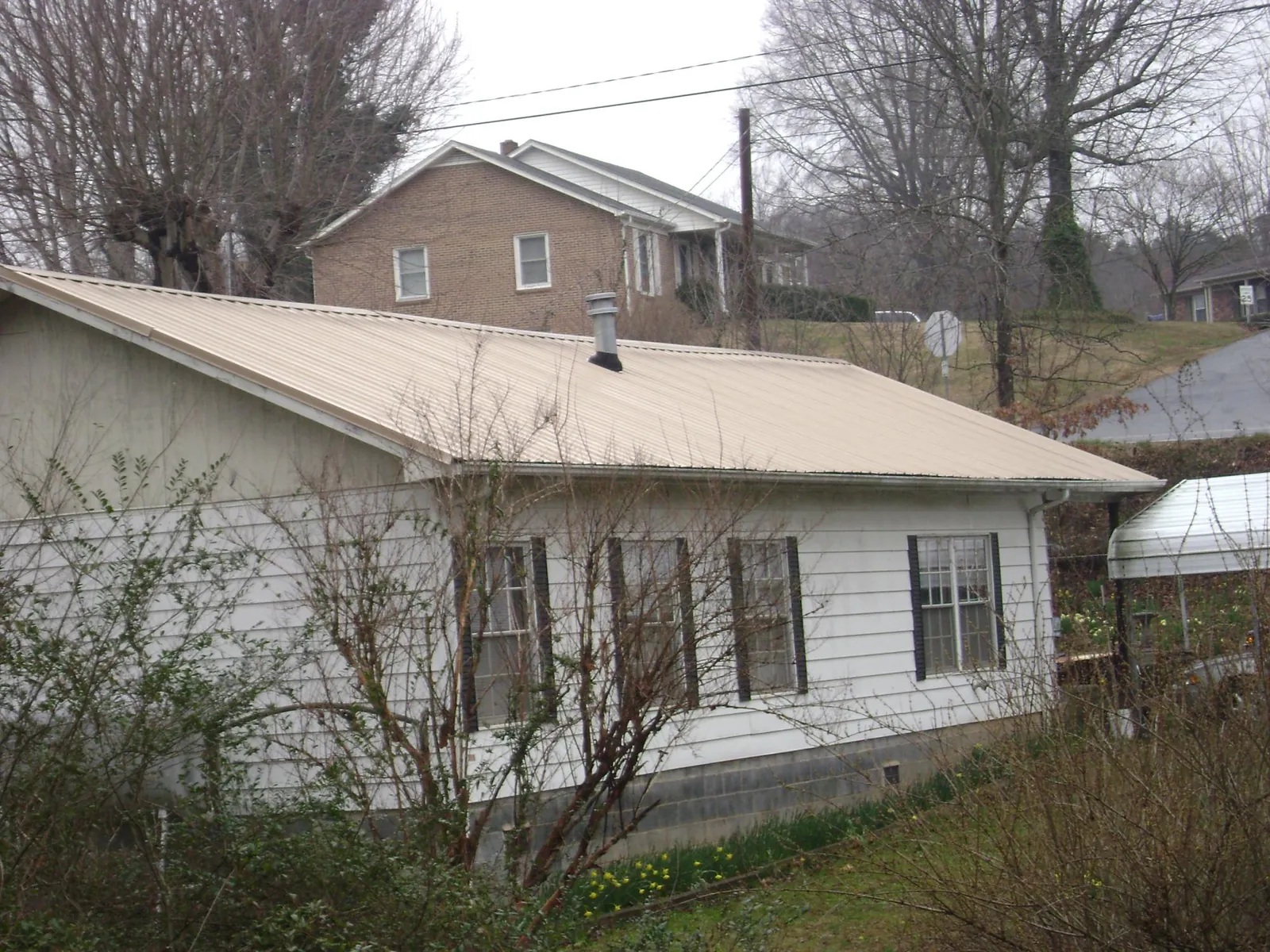 Tan metal roof on a white sided house set into a hillside — Commercial Roofing by Roofing Brothers in Asbury Park